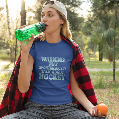 Woman sitting outdoors drinking from a green bottle, wearing a blue t-shirt with text