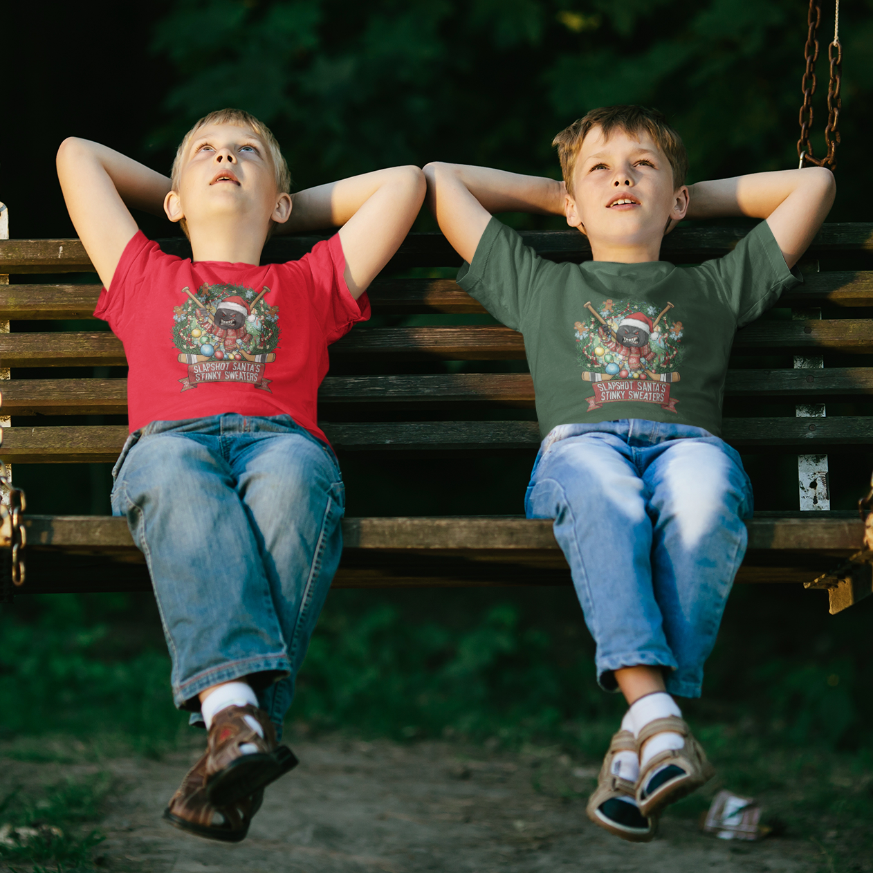 Two children sitting on a swing gazing up at evening stars. They wear shirts with an angry puck and hockey sticks surrounded by evergreen boughs, ornaments and gingerbread men. The caption reads, "Slapshot Santa's Stinky Sweaters."
